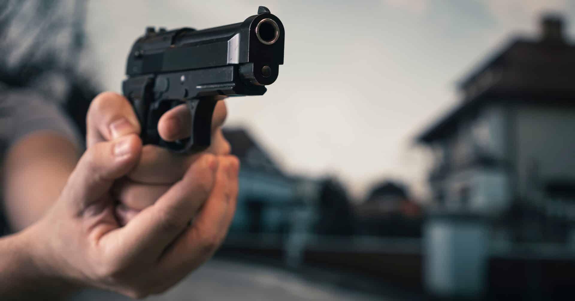 Man pointing a gun at another person in a threatening manner.